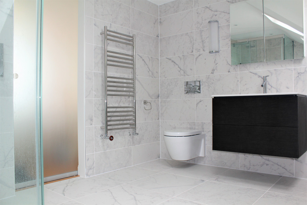 Photo of a large contemporary grey and black ensuite bathroom in Sussex with flat-panel cabinets, black cabinets, a built-in bath, a corner shower, a wall mounted toilet, multi-coloured tiles, porcelain tiles, white walls, porcelain flooring, a built-in sink, solid surface worktops, white floors, a sliding door, white worktops, a wall niche, a single sink, a floating vanity unit and a vaulted ceiling.
