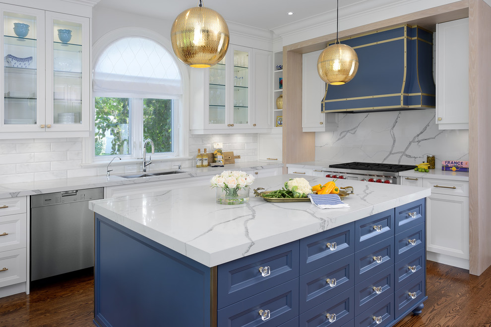 Inspiration for a transitional l-shaped kitchen in Toronto with a double-bowl sink, recessed-panel cabinets, white cabinets, white splashback, stone slab splashback, stainless steel appliances, medium hardwood floors, with island, brown floor and white benchtop.