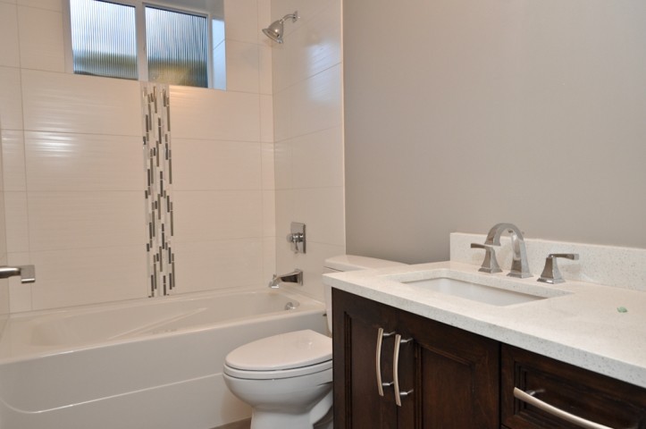 This is an example of a small transitional kids bathroom in Vancouver with recessed-panel cabinets, dark wood cabinets, an alcove tub, a shower/bathtub combo, a two-piece toilet, black tile, gray tile, white tile, porcelain tile, grey walls, an undermount sink, engineered quartz benchtops, a shower curtain and white benchtops.