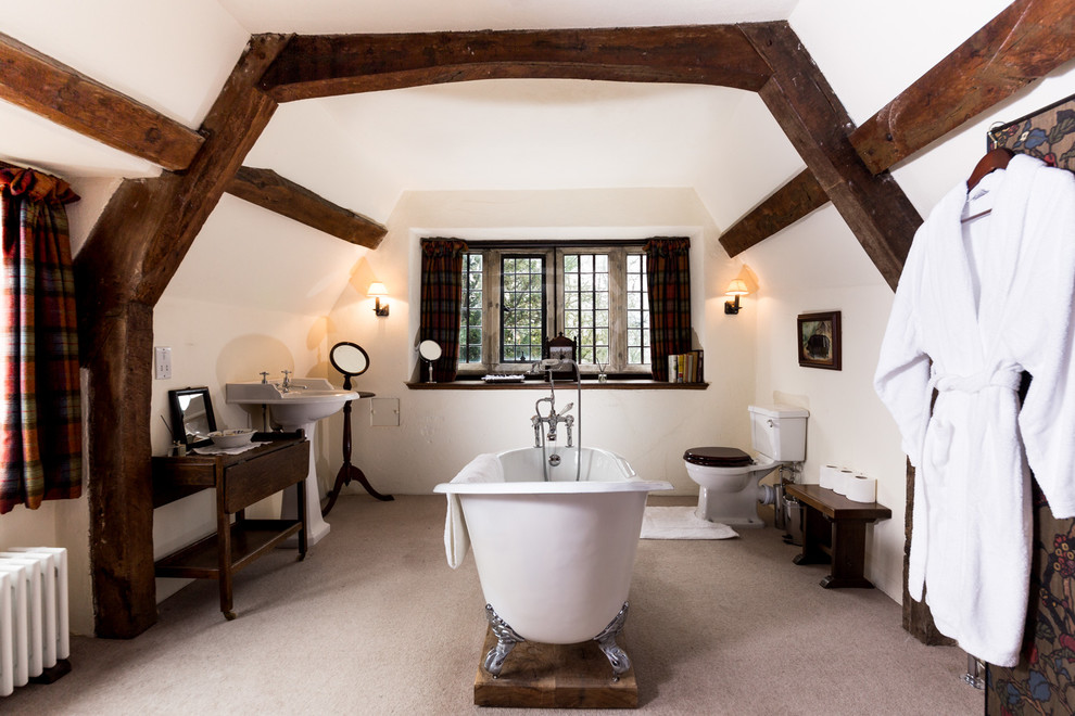Photo of a country master bathroom in Dorset with dark wood cabinets, a claw-foot tub, a two-piece toilet, white walls and a pedestal sink.