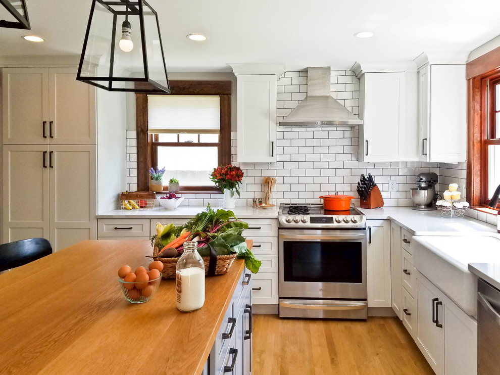 Photo of a country kitchen in Boston with a farmhouse sink, shaker cabinets, white cabinets, quartz benchtops, white splashback, subway tile splashback and stainless steel appliances.