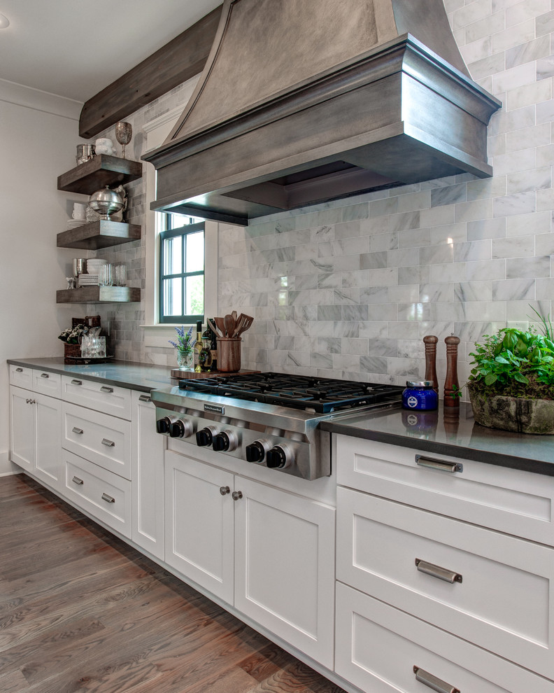 Inspiration for a large transitional l-shaped open plan kitchen in Little Rock with with island, a farmhouse sink, shaker cabinets, white cabinets, granite benchtops, grey splashback, stone tile splashback, stainless steel appliances and medium hardwood floors.