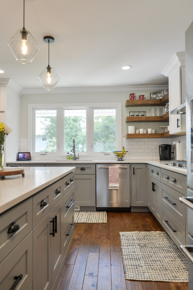 Design ideas for a large transitional l-shaped kitchen in Philadelphia with a drop-in sink, shaker cabinets, grey cabinets, white splashback, subway tile splashback, stainless steel appliances, medium hardwood floors, with island, brown floor and white benchtop.