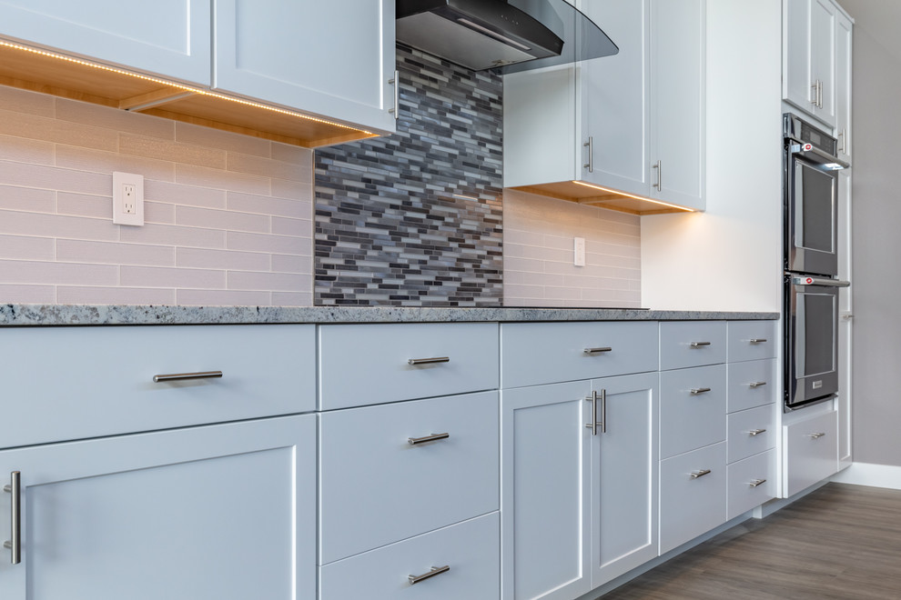 Inspiration for a modern gray floor kitchen remodel in Seattle with shaker cabinets, white cabinets, granite countertops, gray backsplash, matchstick tile backsplash, stainless steel appliances, an island and white countertops