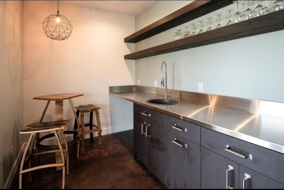 Photo of a small industrial galley wet bar in Salt Lake City with a drop-in sink, flat-panel cabinets, dark wood cabinets, stainless steel benchtops, concrete floors and multi-coloured floor.