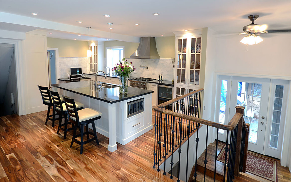 Example of a mid-sized transitional l-shaped medium tone wood floor eat-in kitchen design in Toronto with a double-bowl sink, raised-panel cabinets, white cabinets, solid surface countertops, black backsplash, stone slab backsplash, stainless steel appliances and an island