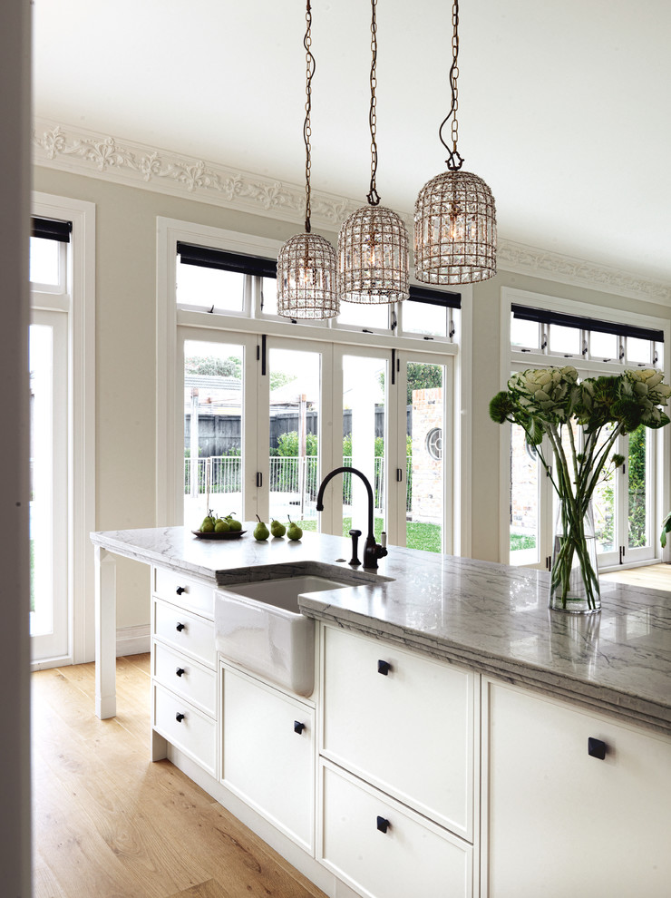 Inspiration for a large traditional l-shaped kitchen in Auckland with a farmhouse sink, raised-panel cabinets, white cabinets, quartzite benchtops, white splashback, white appliances, light hardwood floors and multiple islands.