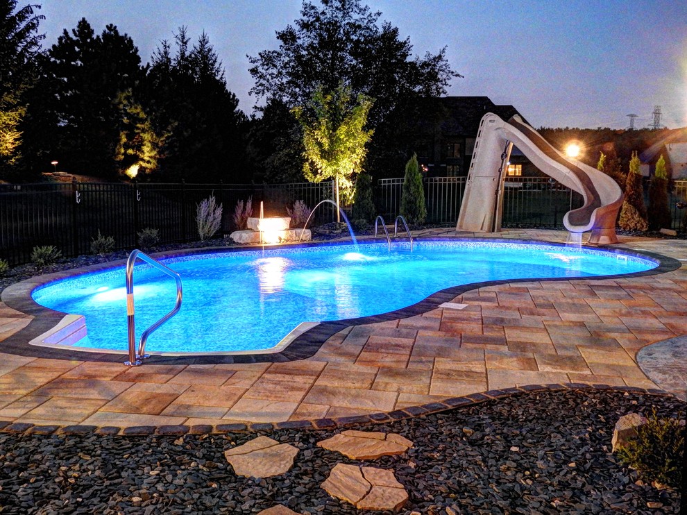 This is an example of a backyard kidney-shaped pool in Chicago with a water slide and brick pavers.