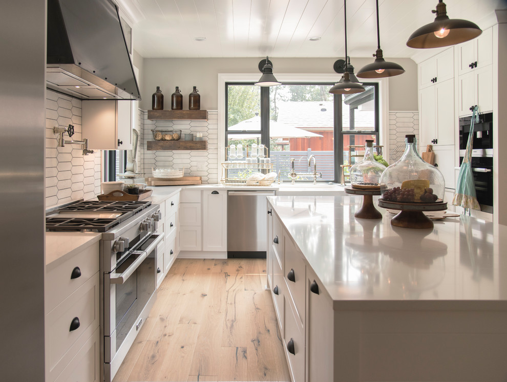 Design ideas for a country u-shaped kitchen in Seattle with a farmhouse sink, shaker cabinets, white cabinets, white splashback, stainless steel appliances, medium hardwood floors, with island, brown floor and white benchtop.