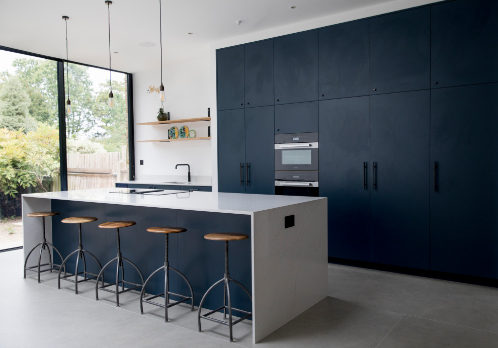 This is an example of an expansive modern galley open plan kitchen in London with an integrated sink, flat-panel cabinets, blue cabinets, quartzite benchtops, cement tiles, with island, grey floor and white benchtop.