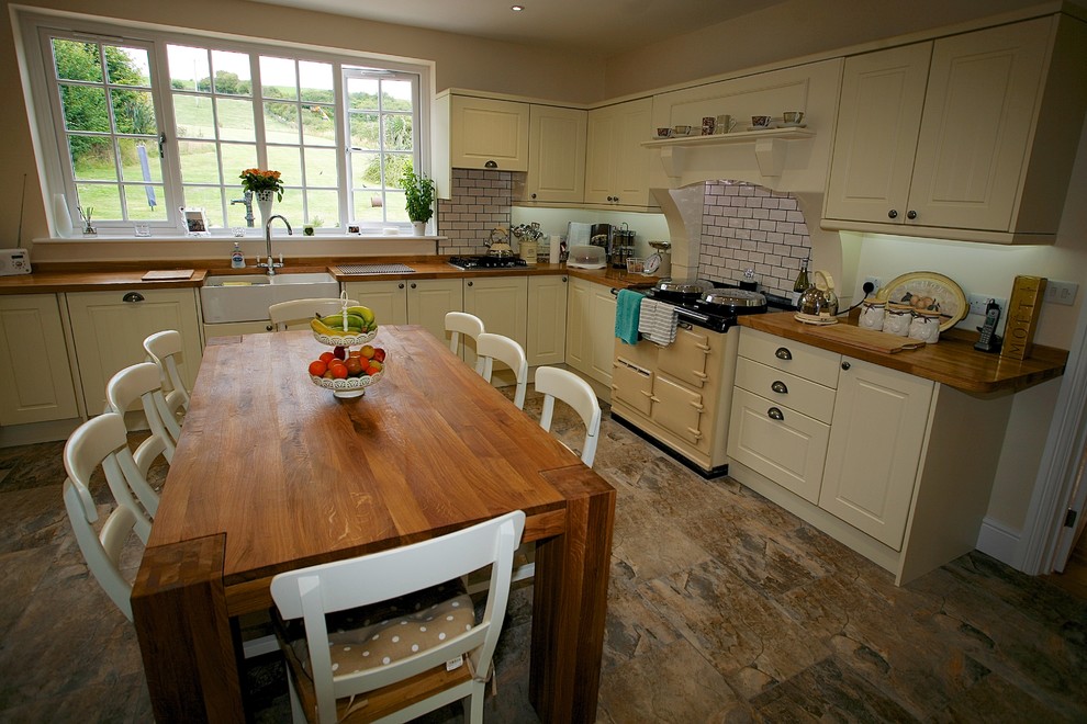 This is an example of a large country l-shaped eat-in kitchen in Dorset with a double-bowl sink, beaded inset cabinets, beige cabinets, wood benchtops, white splashback, ceramic splashback, ceramic floors, with island and brown floor.