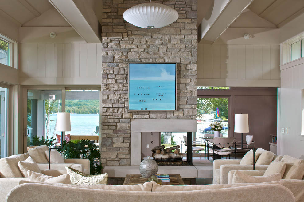 Photo of a beach style living room in Other with a two-sided fireplace and a stone fireplace surround.