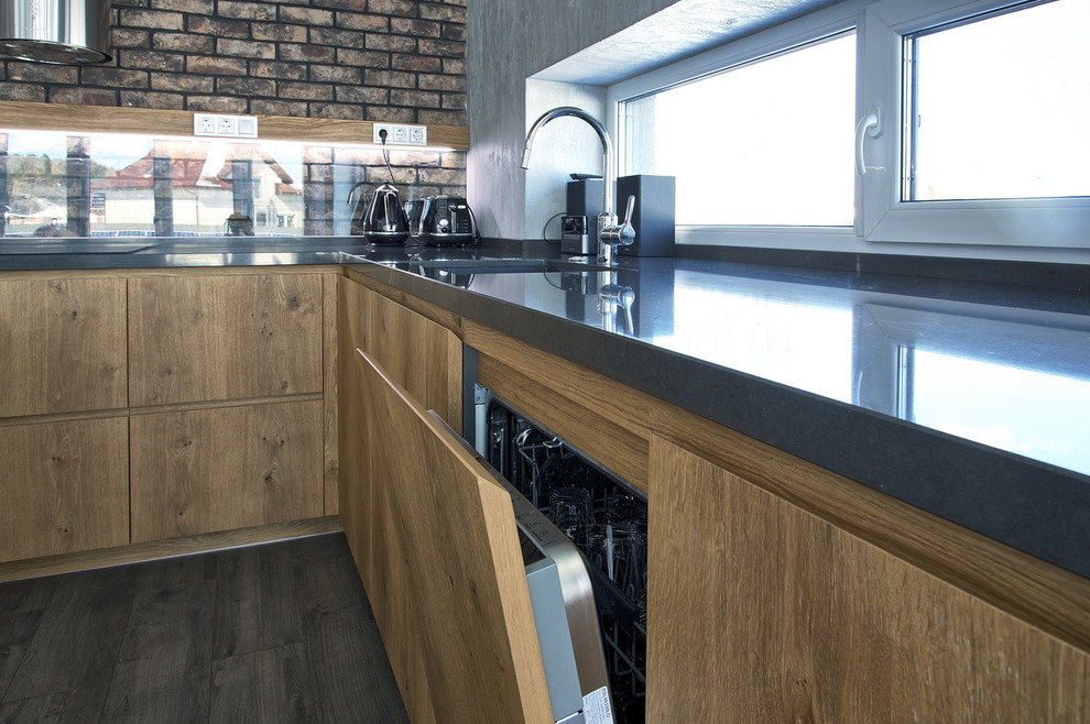 Photo of a large industrial l-shaped eat-in kitchen in Other with a drop-in sink, flat-panel cabinets, medium wood cabinets, quartzite benchtops, brown splashback, brick splashback, black appliances, dark hardwood floors, with island, brown floor and grey benchtop.