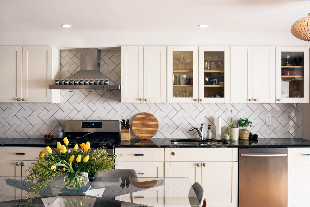 Design ideas for a transitional eat-in kitchen in New York with white splashback, stainless steel appliances, no island, an undermount sink, glass-front cabinets, beige cabinets and ceramic splashback.