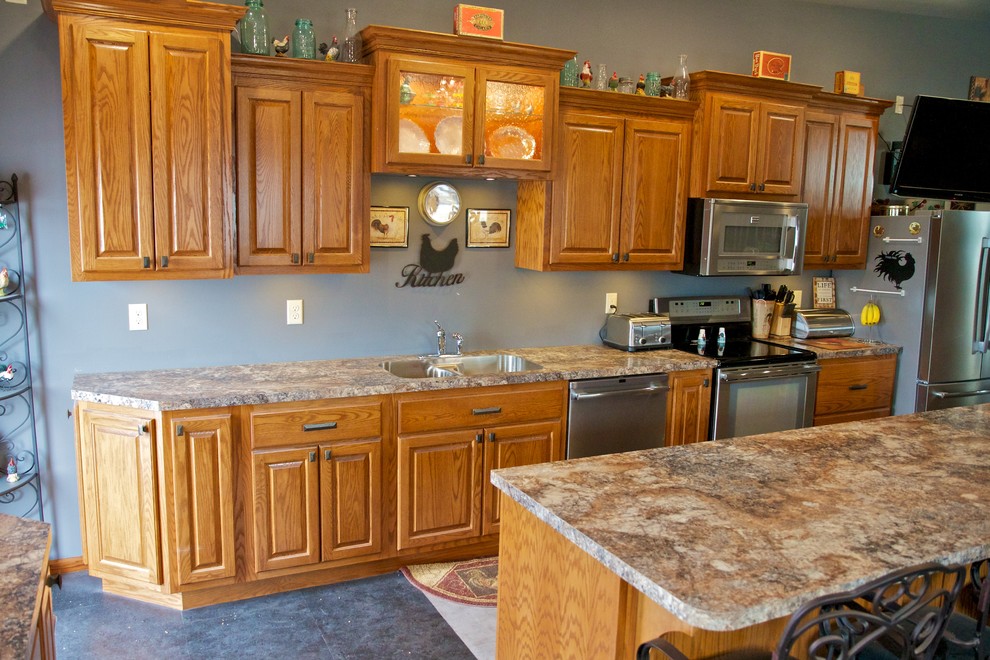 Example of a large l-shaped open concept kitchen design with an undermount sink, raised-panel cabinets, light wood cabinets, laminate countertops, stainless steel appliances and an island