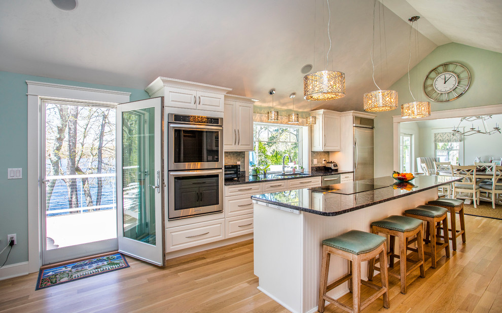 Inspiration for a beach style galley separate kitchen in Boston with raised-panel cabinets, white cabinets, black appliances, medium hardwood floors, with island and brown floor.