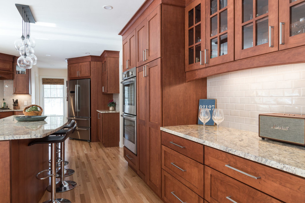 Mid-sized transitional galley eat-in kitchen in Boston with a farmhouse sink, shaker cabinets, medium wood cabinets, granite benchtops, grey splashback, subway tile splashback, stainless steel appliances, medium hardwood floors, with island, brown floor and beige benchtop.