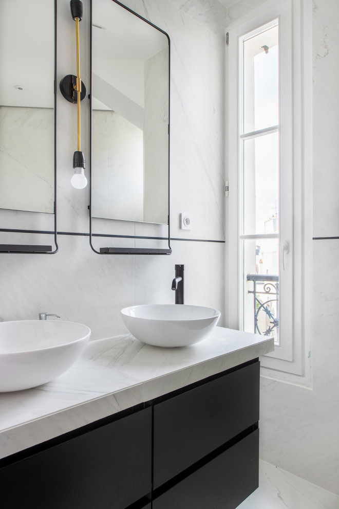 Пример оригинального дизайна: большая главная ванная комната в современном стиле с плоскими фасадами, черными фасадами, отдельно стоящей ванной, душем без бортиков, инсталляцией, белой плиткой, мраморной плиткой, белыми стенами, мраморным полом, настольной раковиной, мраморной столешницей, белым полом, душем с раздвижными дверями, белой столешницей, нишей, тумбой под две раковины и подвесной тумбой