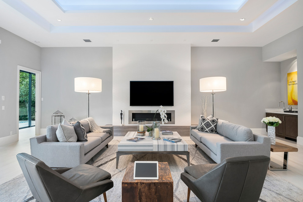 Large contemporary open concept living room in Miami with white walls, porcelain floors, a ribbon fireplace, a tile fireplace surround, a wall-mounted tv, white floor and a home bar.
