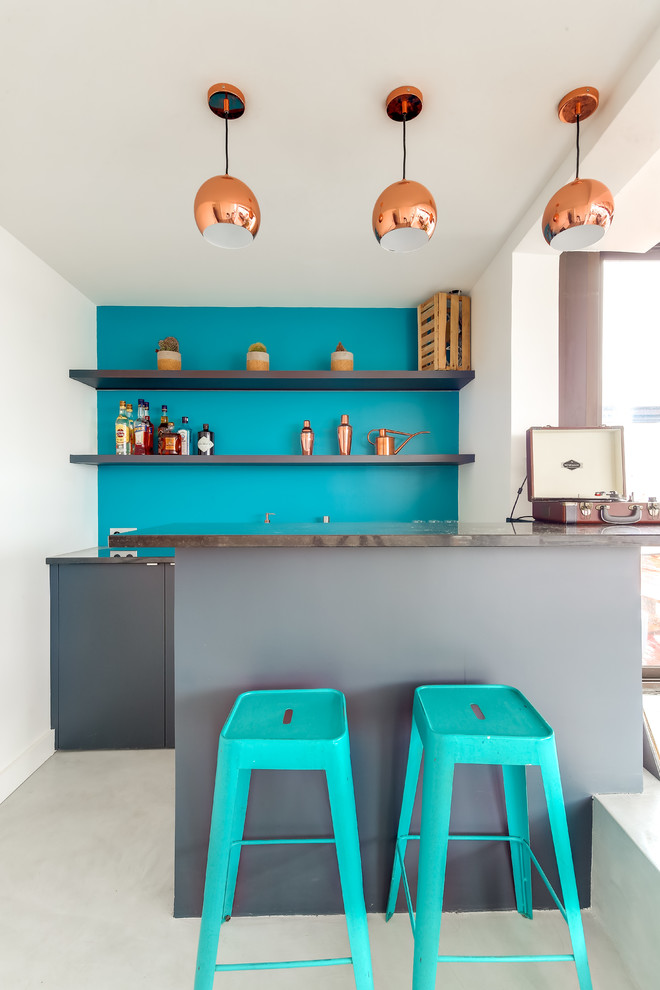 Photo of a small contemporary galley seated home bar in Paris with a drop-in sink, beaded inset cabinets, grey cabinets, granite benchtops, blue splashback, concrete floors, grey floor and black benchtop.