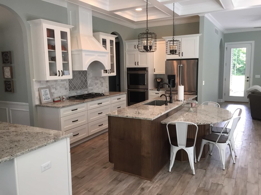 This is an example of a mid-sized transitional galley eat-in kitchen in Detroit with a single-bowl sink, recessed-panel cabinets, white cabinets, granite benchtops, multi-coloured splashback, ceramic splashback, stainless steel appliances, plywood floors, with island and grey floor.