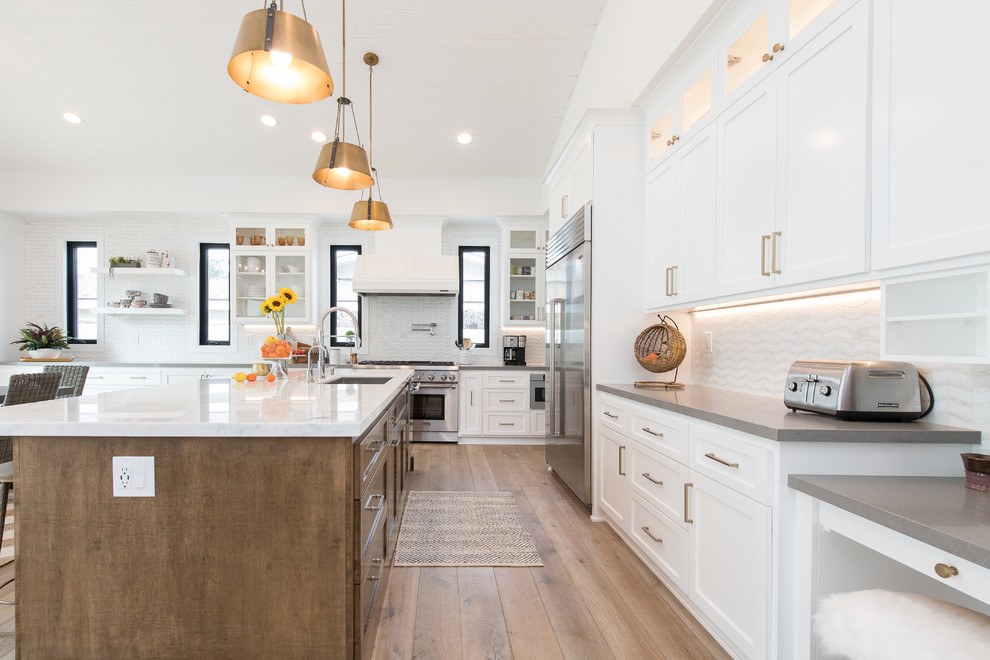 Transitional l-shaped kitchen in Orange County with an undermount sink, shaker cabinets, white cabinets, white splashback, stainless steel appliances, medium hardwood floors, with island, brown floor and grey benchtop.