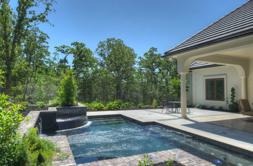 This is an example of a mid-sized traditional backyard custom-shaped lap pool in Dallas with a water feature and concrete pavers.