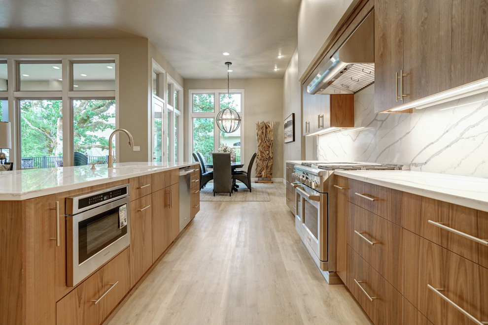 This is an example of a mid-sized contemporary galley kitchen in Portland with an undermount sink, flat-panel cabinets, medium wood cabinets, quartzite benchtops, white splashback, stone slab splashback, stainless steel appliances, light hardwood floors, with island, beige floor and white benchtop.