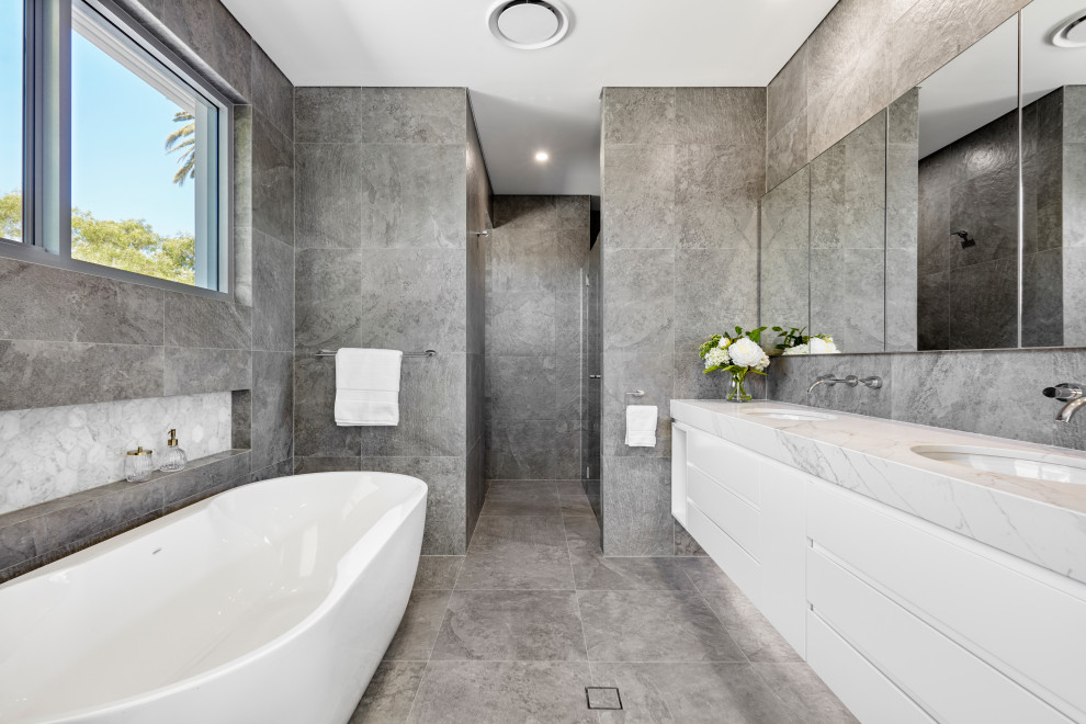 Photo of a mid-sized contemporary master bathroom in Sydney with flat-panel cabinets, white cabinets, a freestanding tub, an alcove shower, gray tile, ceramic tile, grey walls, ceramic floors, an undermount sink, engineered quartz benchtops, grey floor, a hinged shower door, grey benchtops, a double vanity and a floating vanity.