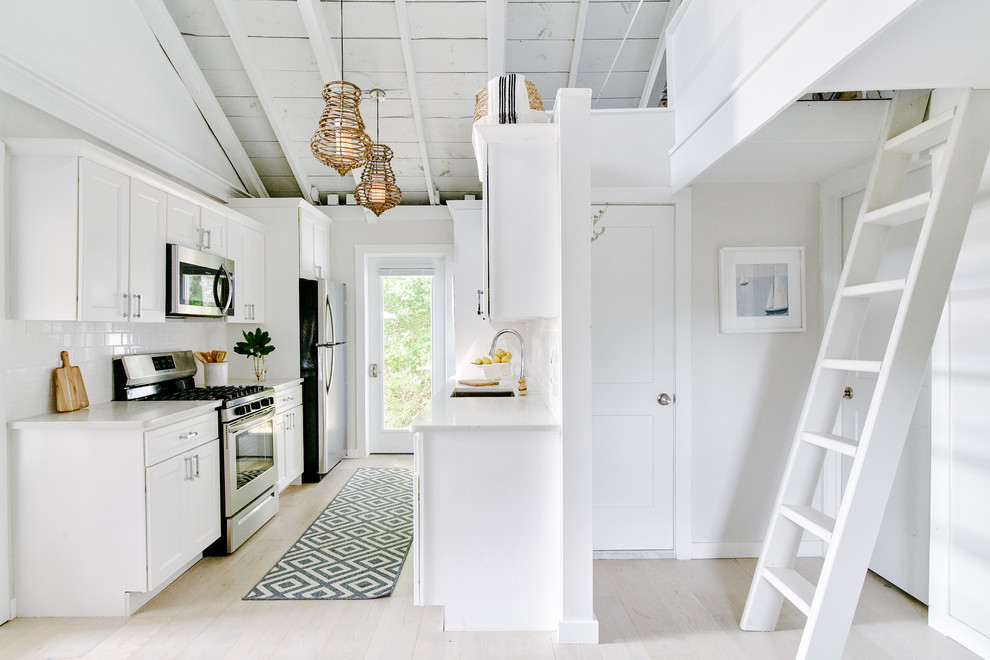 Photo of a small beach style galley kitchen pantry in Providence with a single-bowl sink, recessed-panel cabinets, white cabinets, granite benchtops, white splashback, ceramic splashback, stainless steel appliances, light hardwood floors, no island, beige floor and white benchtop.