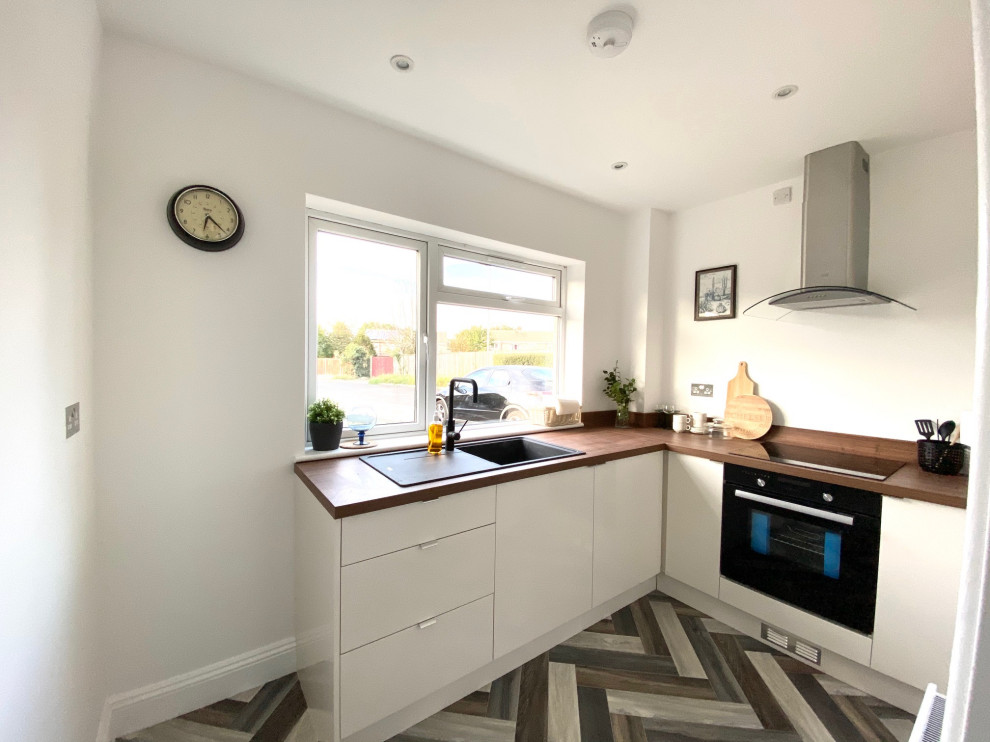 Photo of a small contemporary l-shaped separate kitchen in Gloucestershire with an integrated sink, flat-panel cabinets, white cabinets, wood benchtops, brown splashback, timber splashback, black appliances, linoleum floors, no island, multi-coloured floor and brown benchtop.