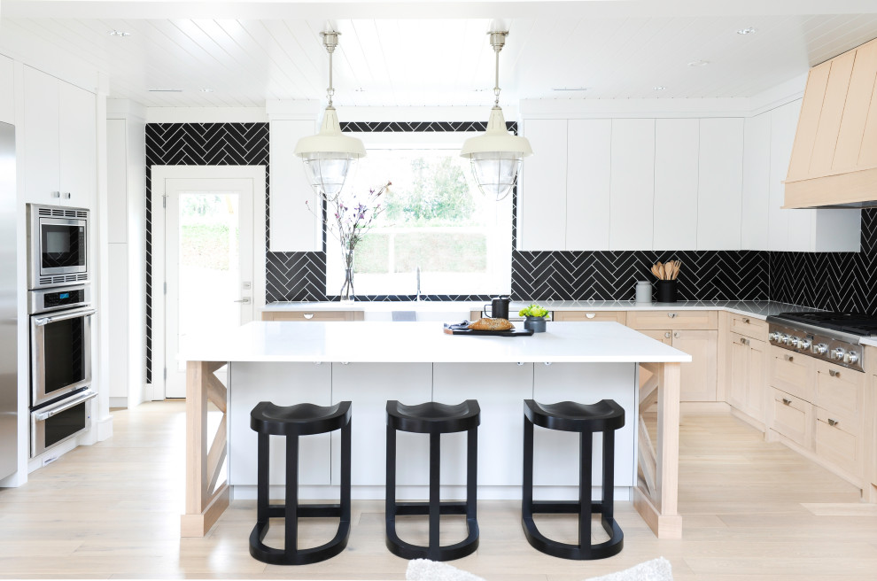 Inspiration for a scandinavian u-shaped open plan kitchen in Other with black splashback, with island, timber, a farmhouse sink, shaker cabinets, light wood cabinets, stainless steel appliances, light hardwood floors, beige floor and white benchtop.