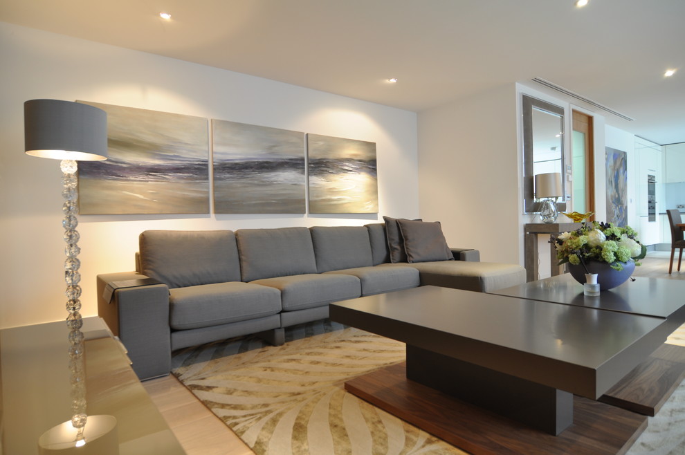 This is an example of a large contemporary open concept living room in London with white walls, light hardwood floors, no fireplace and a freestanding tv.