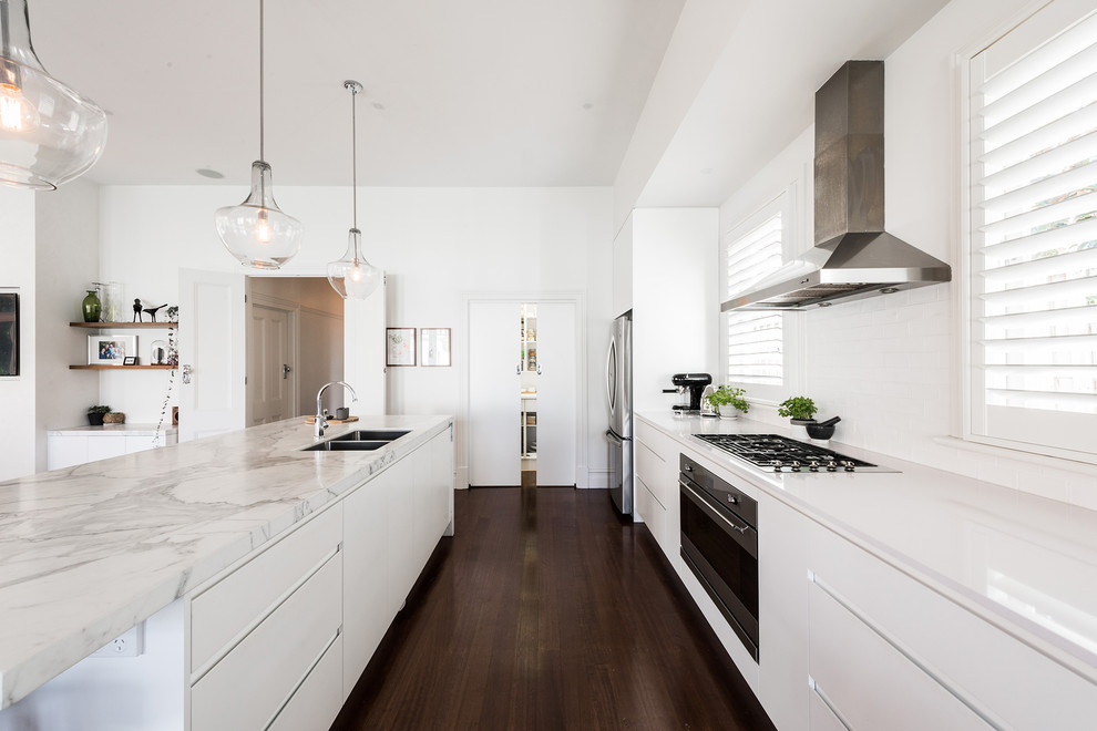 Inspiration for a mid-sized contemporary single-wall open plan kitchen in Melbourne with an undermount sink, flat-panel cabinets, white cabinets, marble benchtops, white splashback, subway tile splashback, stainless steel appliances, dark hardwood floors, with island and brown floor.
