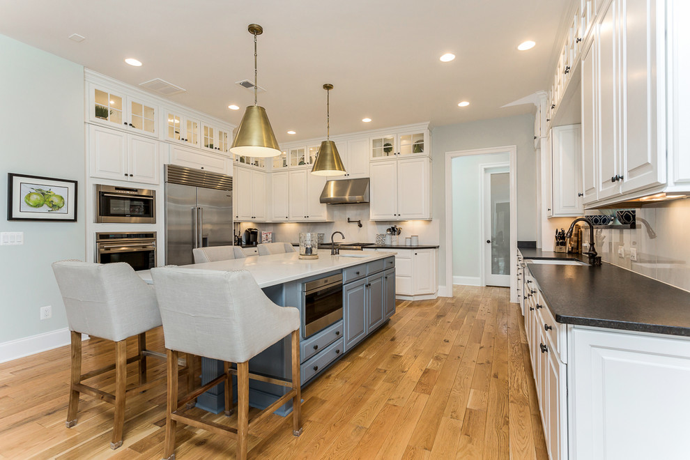 This is an example of a traditional u-shaped kitchen in DC Metro with a farmhouse sink, raised-panel cabinets, white cabinets, stainless steel appliances, medium hardwood floors, with island and brown floor.