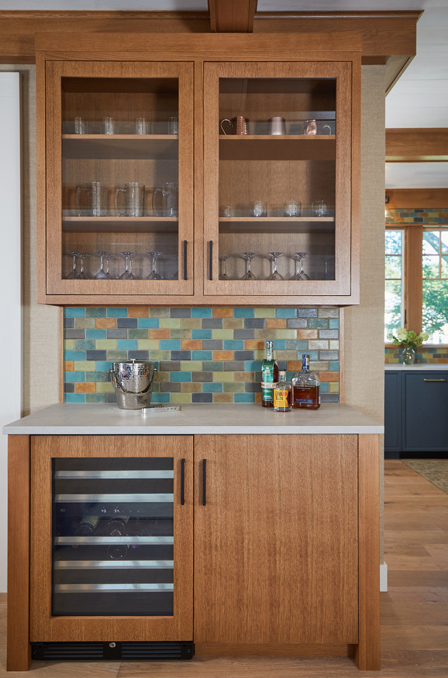 Inspiration for a small arts and crafts single-wall home bar in Grand Rapids with glass-front cabinets, medium wood cabinets, quartz benchtops, multi-coloured splashback, medium hardwood floors and white benchtop.