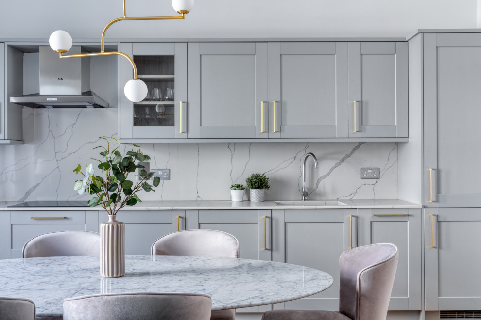 This is an example of a mid-sized transitional single-wall eat-in kitchen in London with an integrated sink, shaker cabinets, blue cabinets, white splashback, no island and white benchtop.