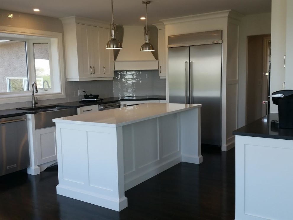 Inspiration for a mid-sized transitional dark wood floor and brown floor kitchen remodel with a farmhouse sink, shaker cabinets, white cabinets, quartz countertops, gray backsplash, subway tile backsplash, stainless steel appliances and an island