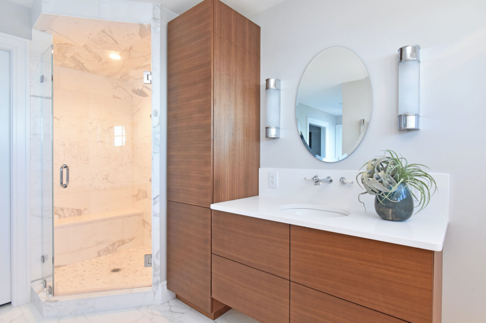 This is an example of a mid-sized modern master bathroom in Providence with flat-panel cabinets, medium wood cabinets, a freestanding tub, a corner shower, white walls, marble floors, an undermount sink, engineered quartz benchtops, white floor, a hinged shower door and white benchtops.
