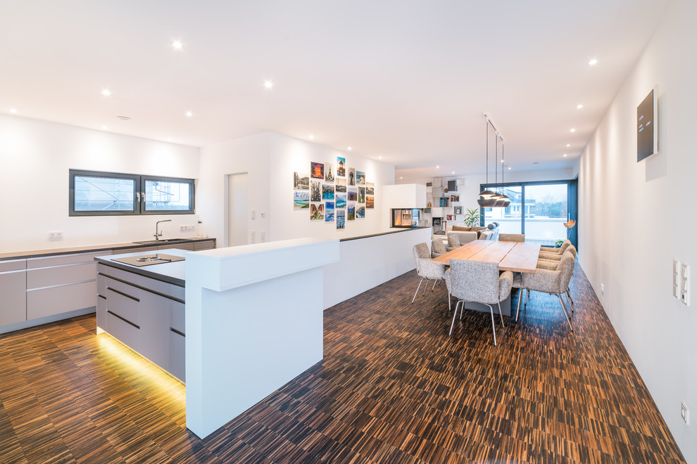 This is an example of a large contemporary kitchen/dining combo in Frankfurt with white walls, bamboo floors, a two-sided fireplace, a plaster fireplace surround and brown floor.