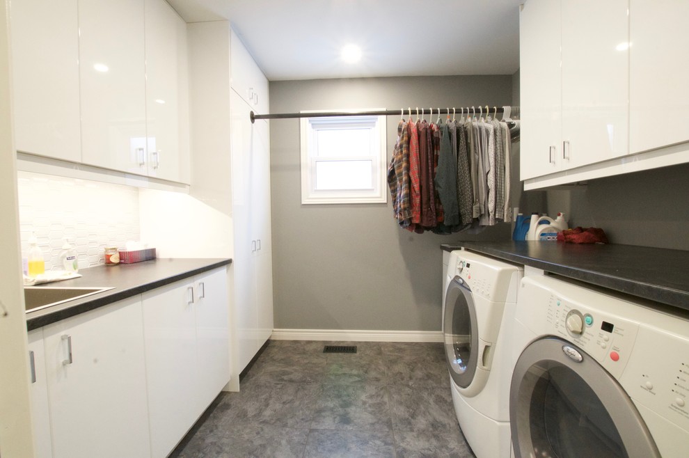 Mid-sized contemporary galley dedicated laundry room in Toronto with an utility sink, glass-front cabinets, white cabinets, laminate benchtops, grey walls, vinyl floors, a side-by-side washer and dryer, black floor and black benchtop.