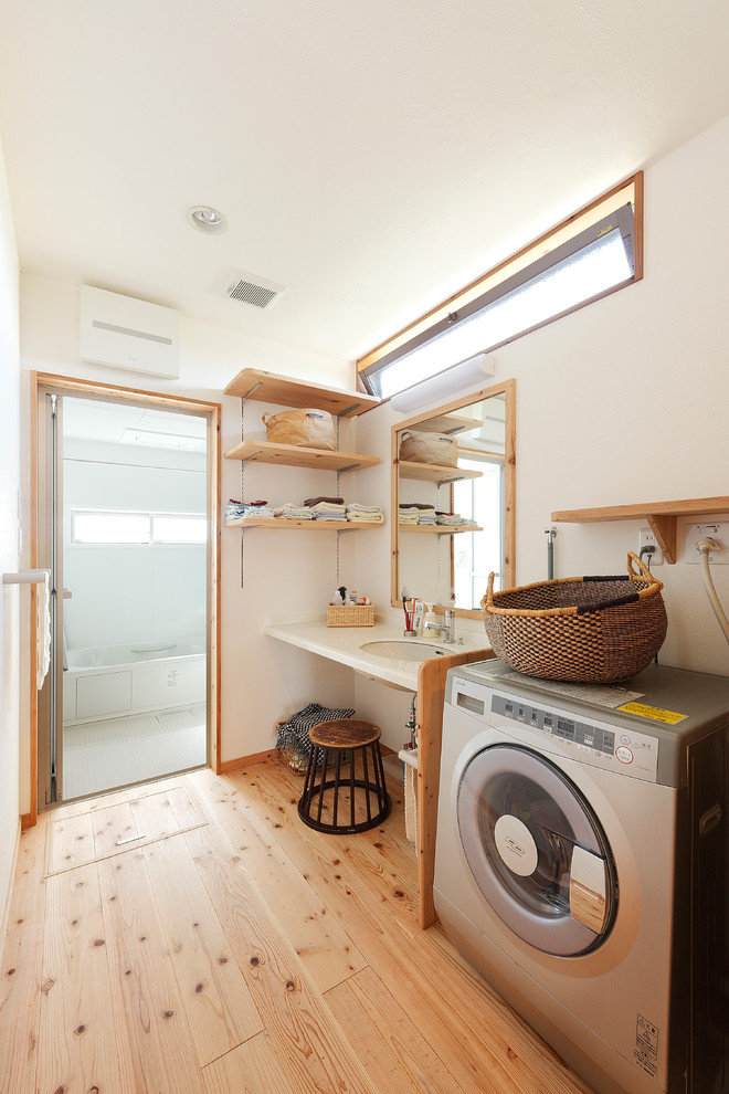 Design ideas for an asian laundry room in Other with white walls, medium hardwood floors, brown floor and an undermount sink.