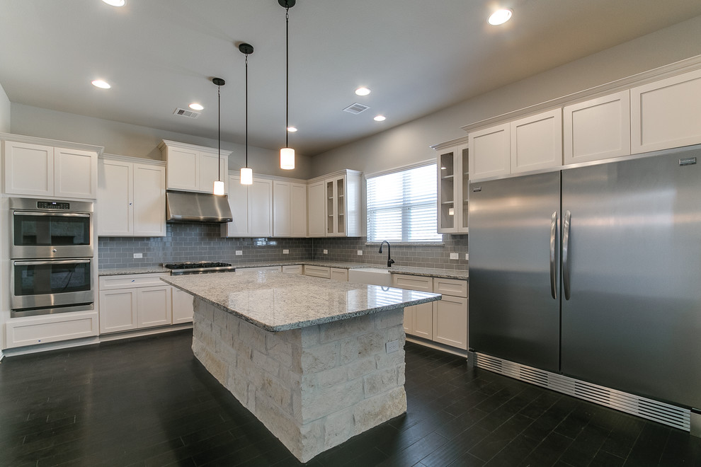 This is an example of a mid-sized traditional eat-in kitchen in Houston with a farmhouse sink, granite benchtops, grey splashback, glass tile splashback, stainless steel appliances, with island, brown floor and grey benchtop.