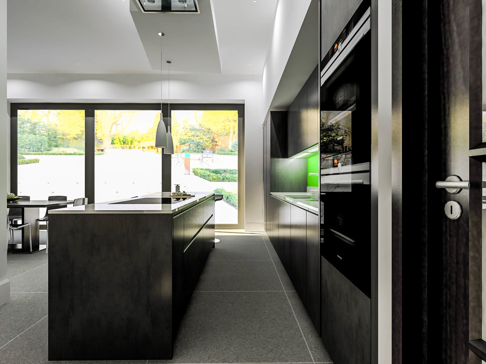 Photo of a mid-sized contemporary single-wall open plan kitchen in London with a single-bowl sink, flat-panel cabinets, grey cabinets, quartzite benchtops, green splashback, glass sheet splashback, black appliances, porcelain floors, with island and grey floor.