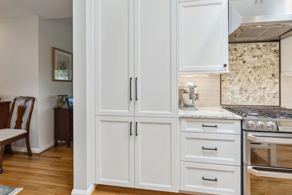 Inredning av ett klassiskt mellanstort vit vitt kök, med en undermonterad diskho, luckor med infälld panel, vita skåp, granitbänkskiva, beige stänkskydd, stänkskydd i keramik, rostfria vitvaror, ljust trägolv, en köksö och brunt golv