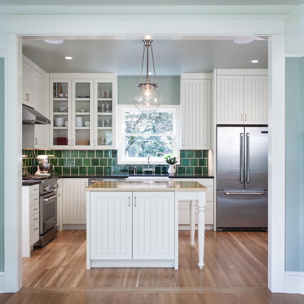 Photo of a mid-sized traditional u-shaped separate kitchen in Portland with a farmhouse sink, white cabinets, granite benchtops, green splashback, ceramic splashback, stainless steel appliances, light hardwood floors, with island and recessed-panel cabinets.