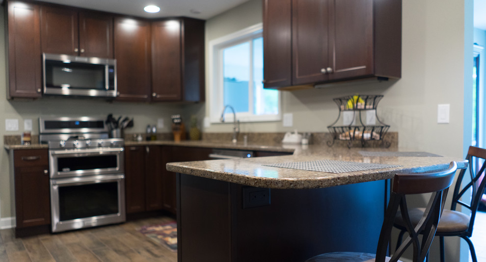 Inspiration for a mid-sized u-shaped ceramic tile enclosed kitchen remodel with an undermount sink, shaker cabinets, dark wood cabinets, quartz countertops, brown backsplash, stainless steel appliances and a peninsula