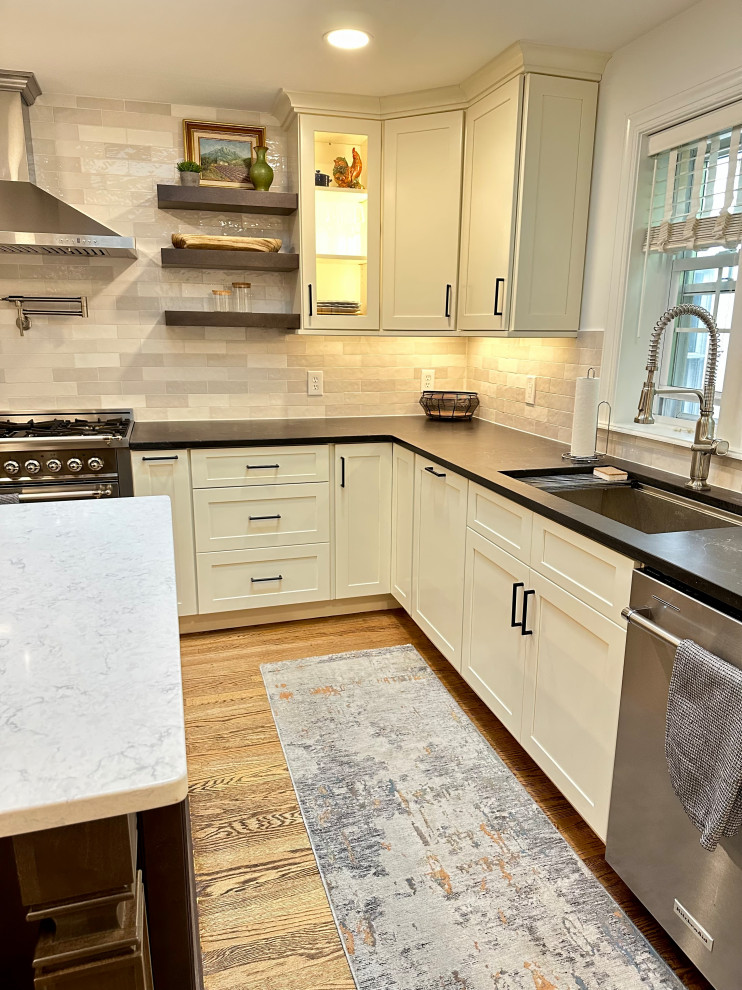 Exempel på ett stort klassiskt vit vitt kök, med en undermonterad diskho, luckor med infälld panel, vita skåp, bänkskiva i kvarts, grått stänkskydd, stänkskydd i porslinskakel, rostfria vitvaror, ljust trägolv, en köksö och brunt golv