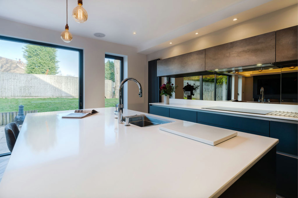 Mid-sized trendy vinyl floor and multicolored floor open concept kitchen photo in West Midlands with a single-bowl sink, flat-panel cabinets, black cabinets, quartzite countertops, metallic backsplash, mirror backsplash, black appliances, an island and white countertops