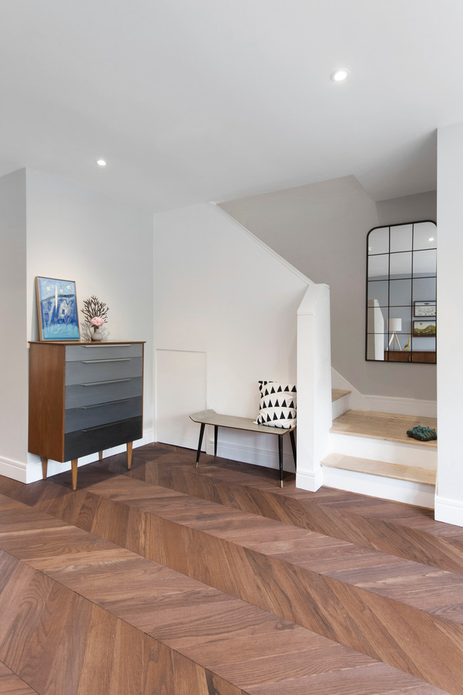 This is an example of a transitional hallway in London with white walls and medium hardwood floors.